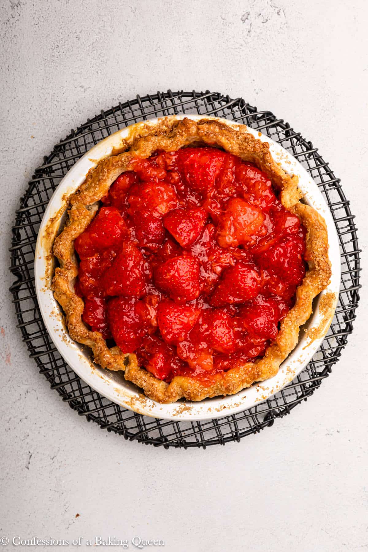 strawberry pie filling added to pie curst on an wire rack on a grey surface