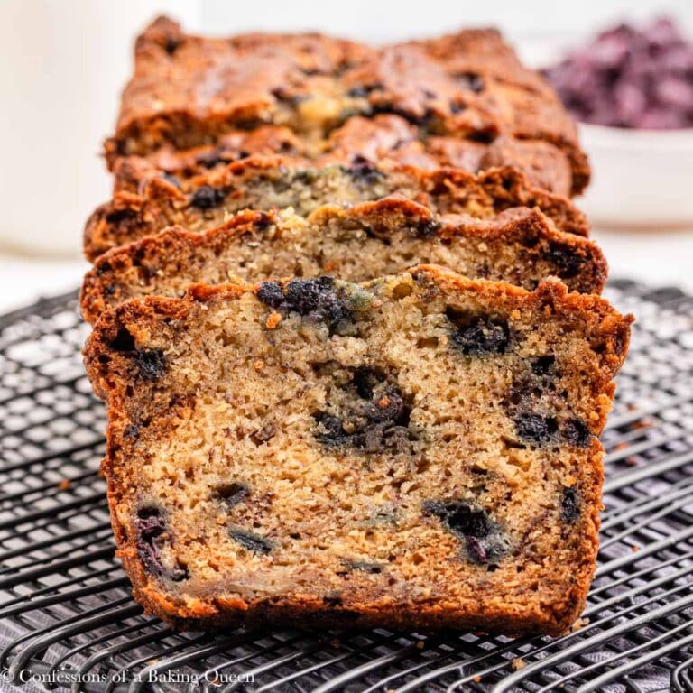 blueberry banana bread sliced on a wire rack on top of a blue linen on a light surface.