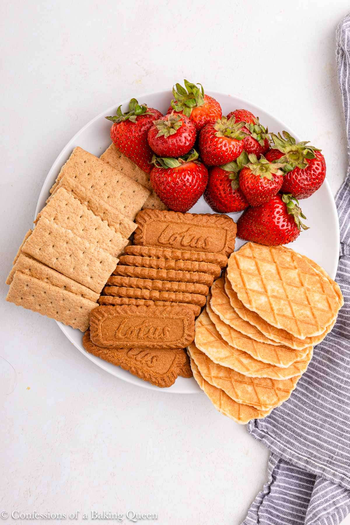 graham crackers, biscuits and strawberries on a white plate on a light surface with a blue linen