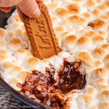 up close of Biscoff cookie dipped into smores dip in an cast iron skillet.