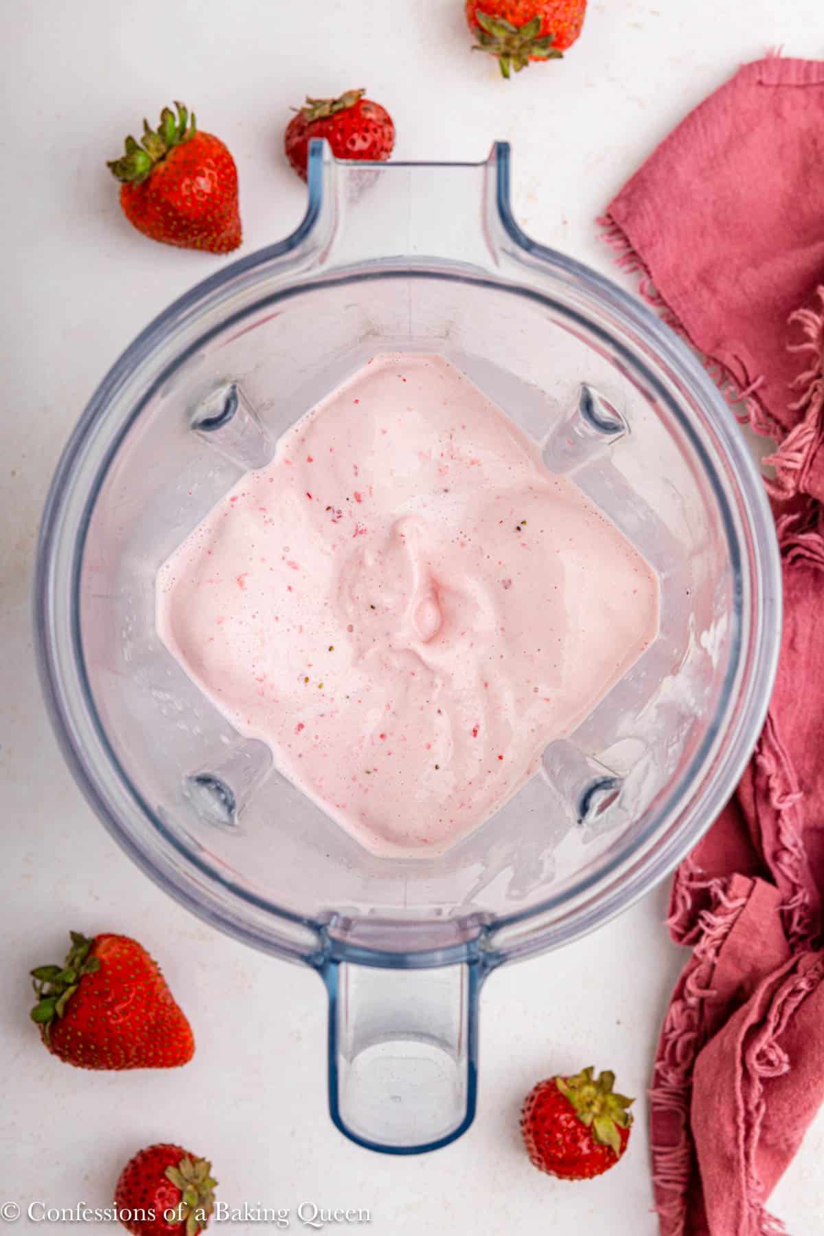 strawberry milkshake in a vitamix blender on a light surface with a pink linen and strawberries