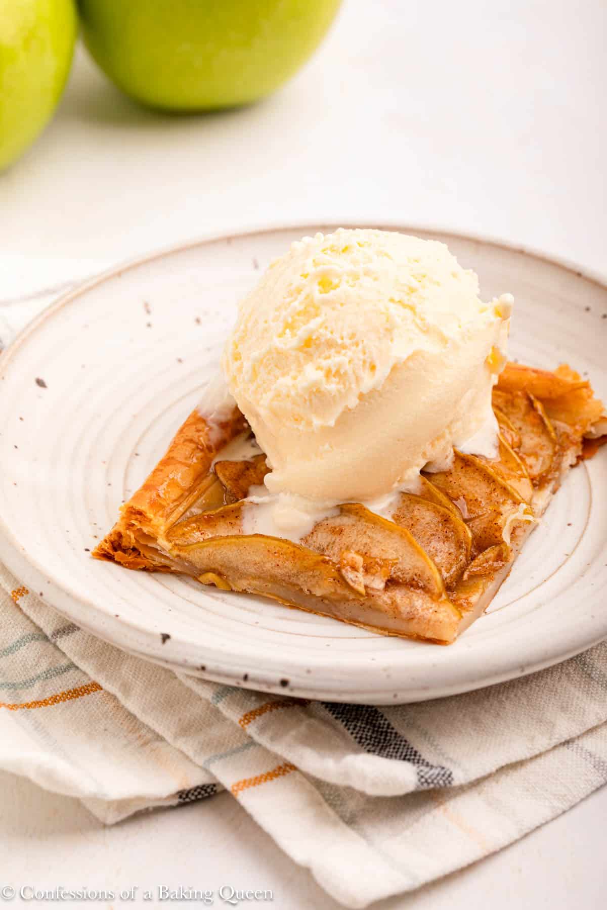 ice cream on top of apple tart on a white plate on top of a stripped linen on a light background