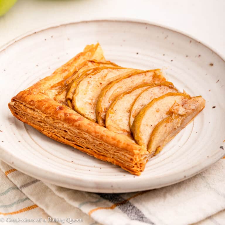 slice of apple tart on a white plate on top of a stripped linen on a light background