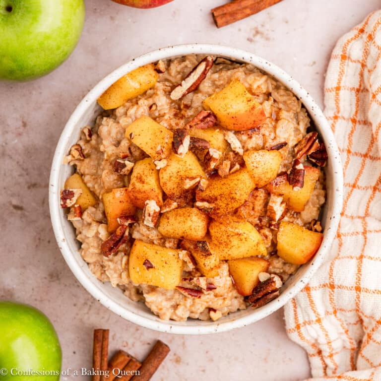 apple cinnamon oatmeal in a large bowl on a light brown surface with apples, cinnamon sticks, and a linen.