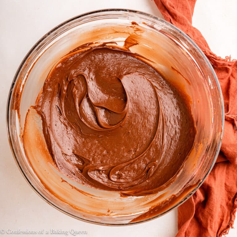 bowl of chocolate sour cream frosting on an light surface with an orange linen.