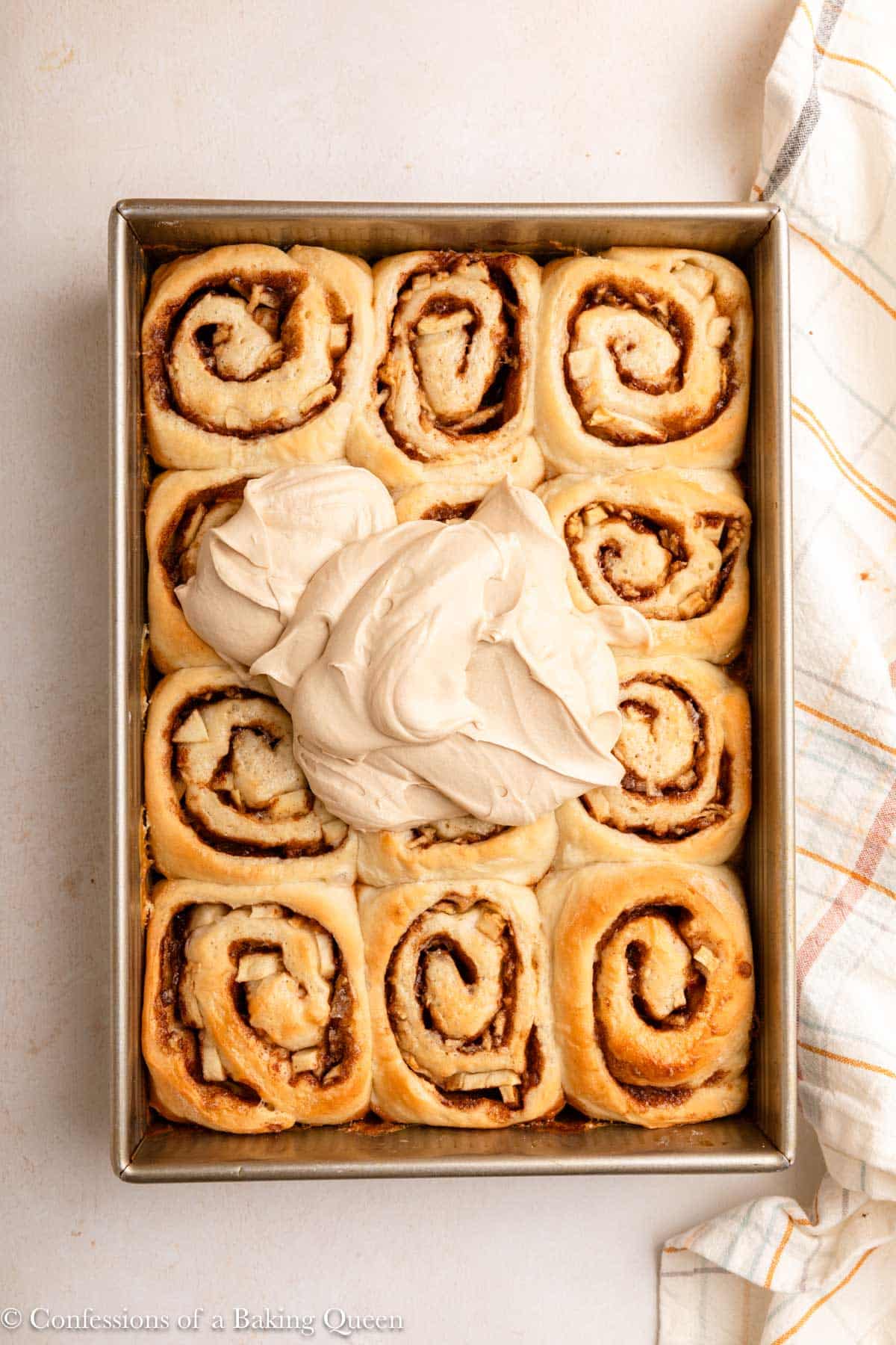 maple frosting on top of apple cinnamon rolls in a metal pan on a light surface with a light colored linen.