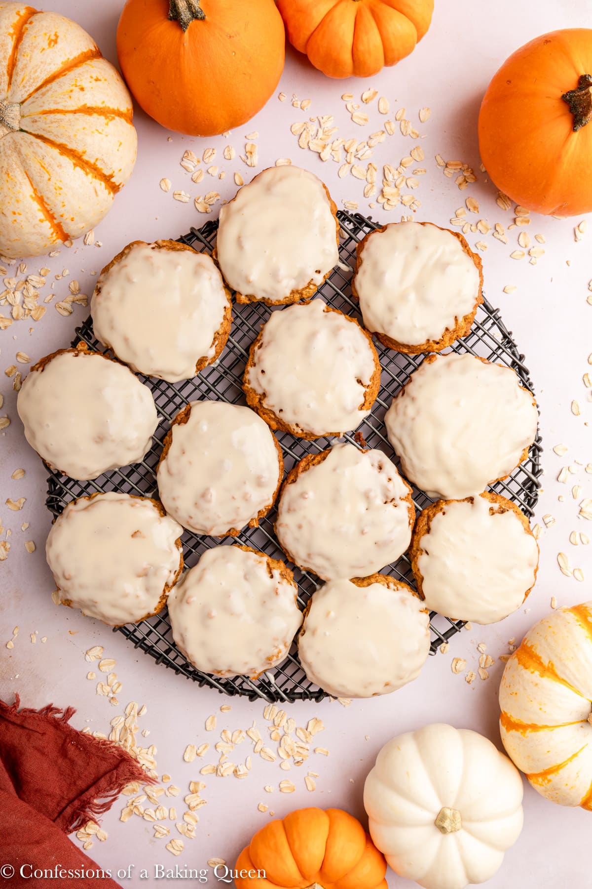 maple glazed pumpkin oatmeal cookies on a wire rack next to some pumpkin on a light surface.