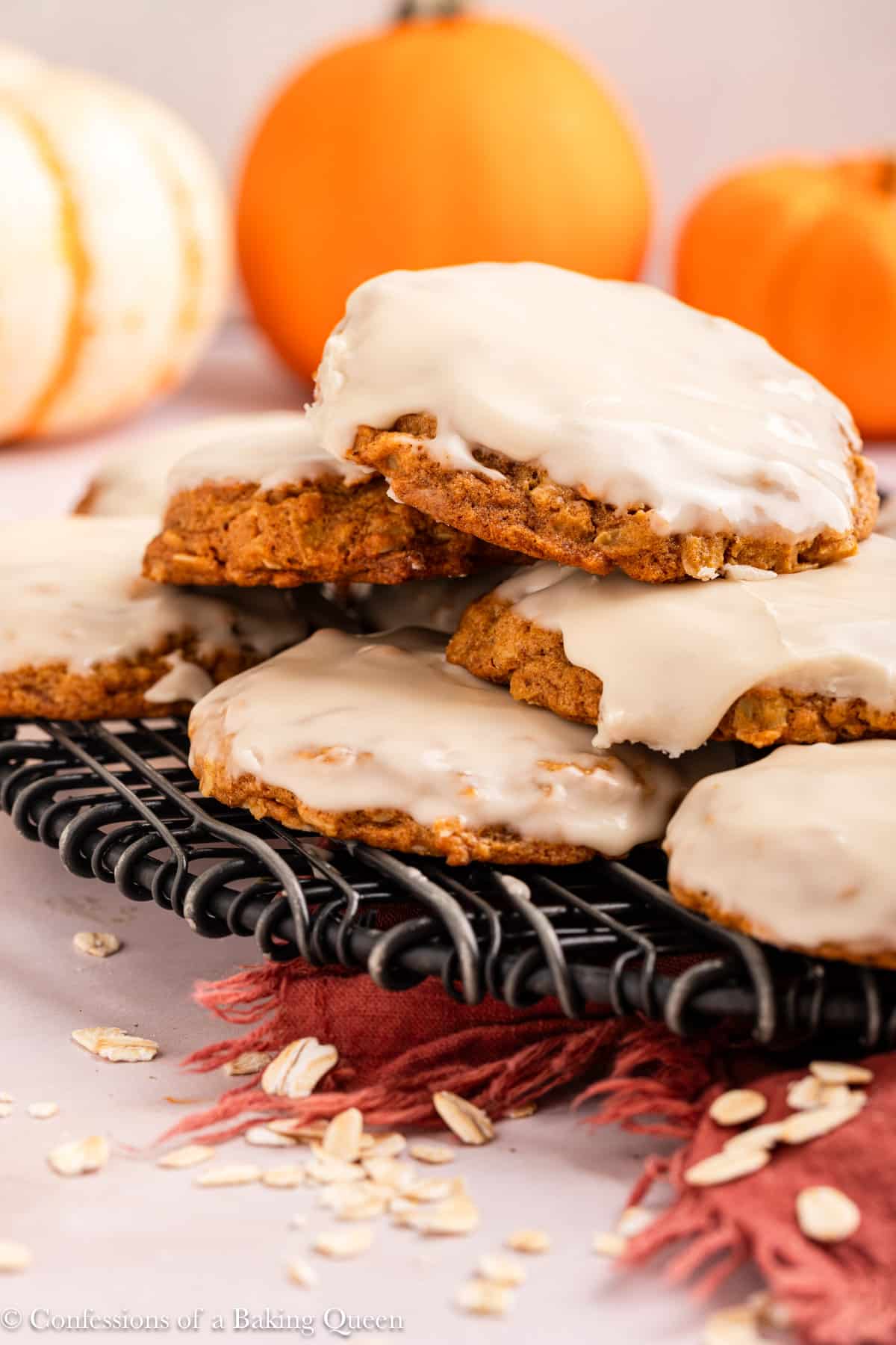 stack of pumpkin oatmeal cookies on a wire rack on a light pink surface with an orange linen.