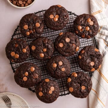 double chocolate banana muffins on a wire rack with a bowl of chocolate chips on a light surface with a light linen.