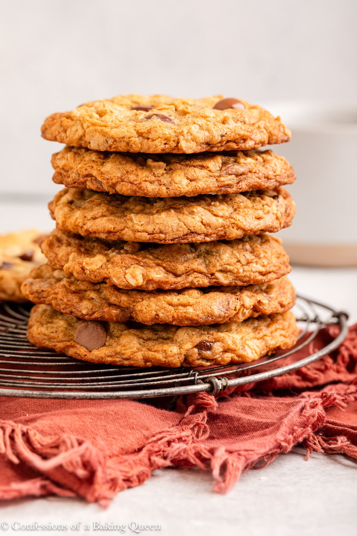 stack of chocolate chip oatmeal cookies on a wire rack on an orange linen with a grey surface.