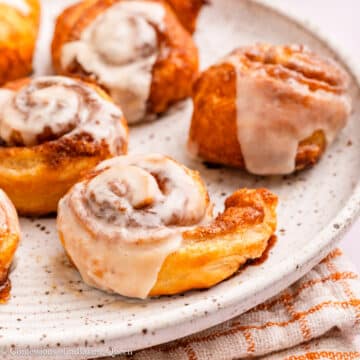 plate full of puff pastry cinnamon rolls on a light surface with a white and orange linen.