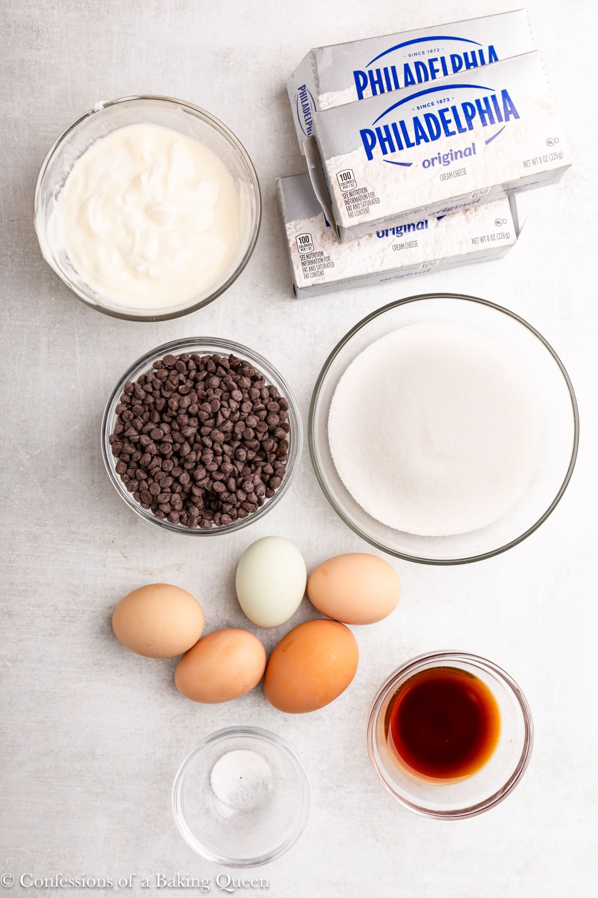 ingredients for chocolate chip cheesecake in small glass bowls on a light grey surface.