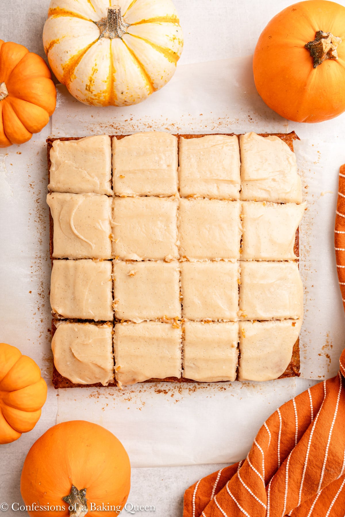 pumpkin snack cake cut into squares on a light grey surface with pumpkin and orange linen.