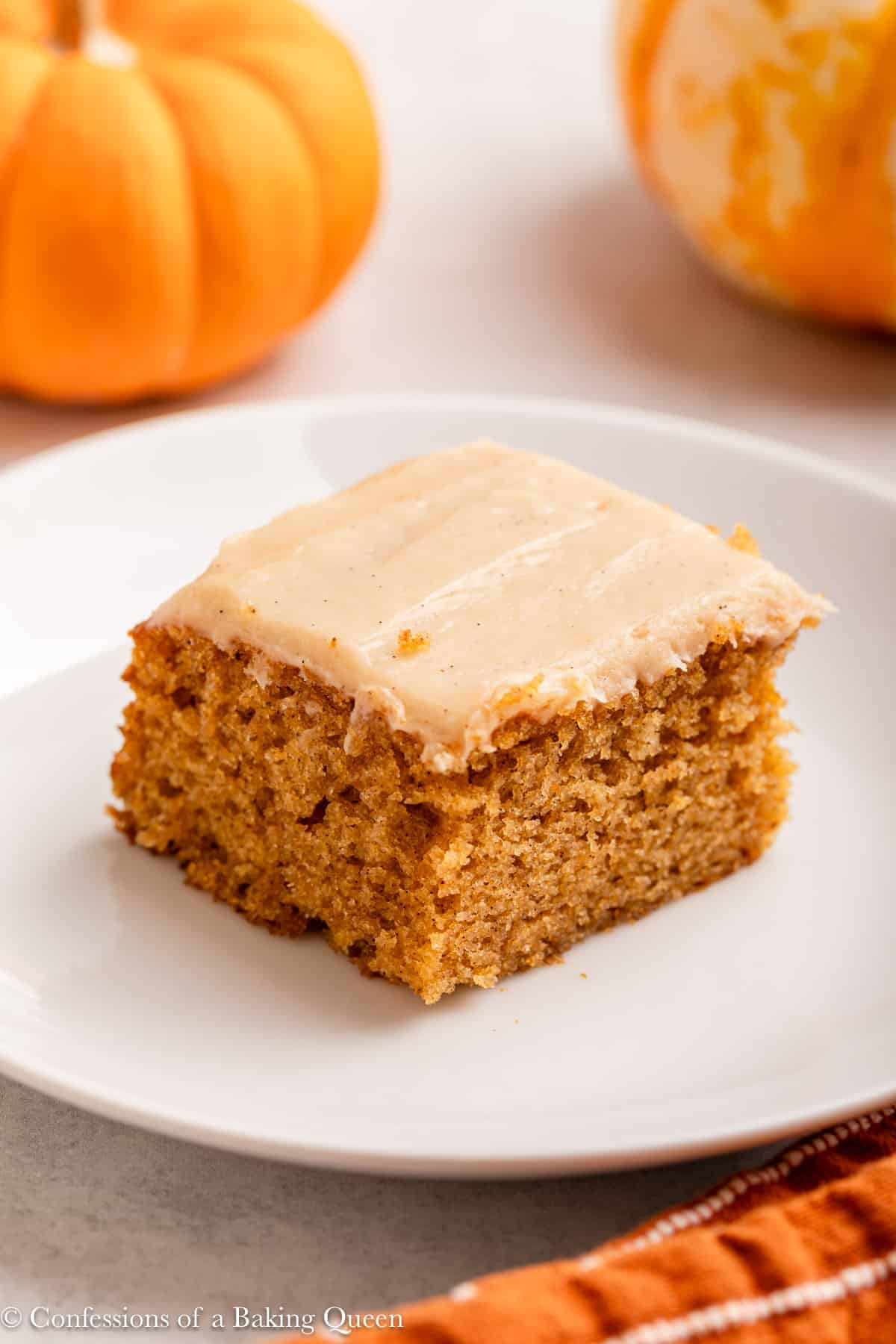 slice of pumpkin spice cake on a white plate on a light grey surface with an orange linen.