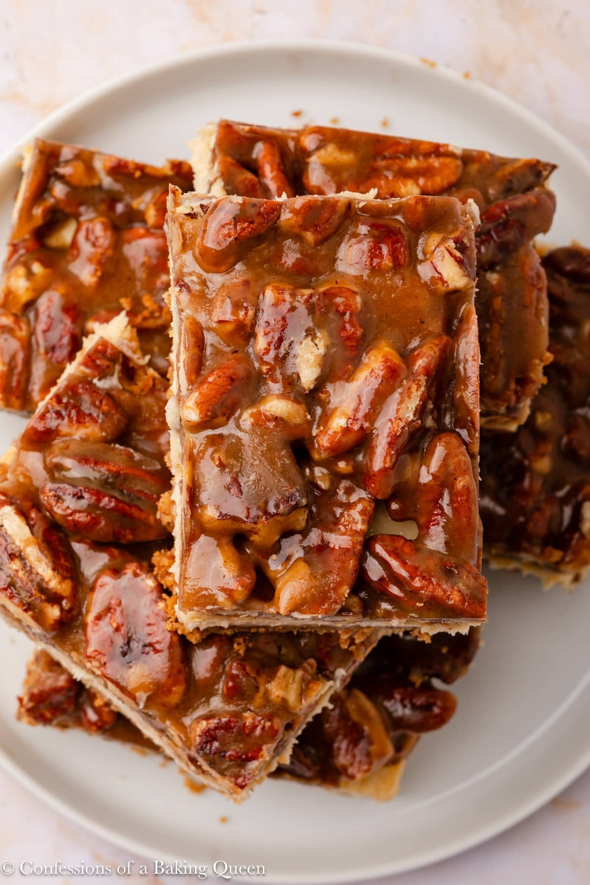 A plate stacked with gooey pecan bars featuring a glossy caramel topping and a crumbly crust, showcasing whole and chopped pecans throughout the dessert.