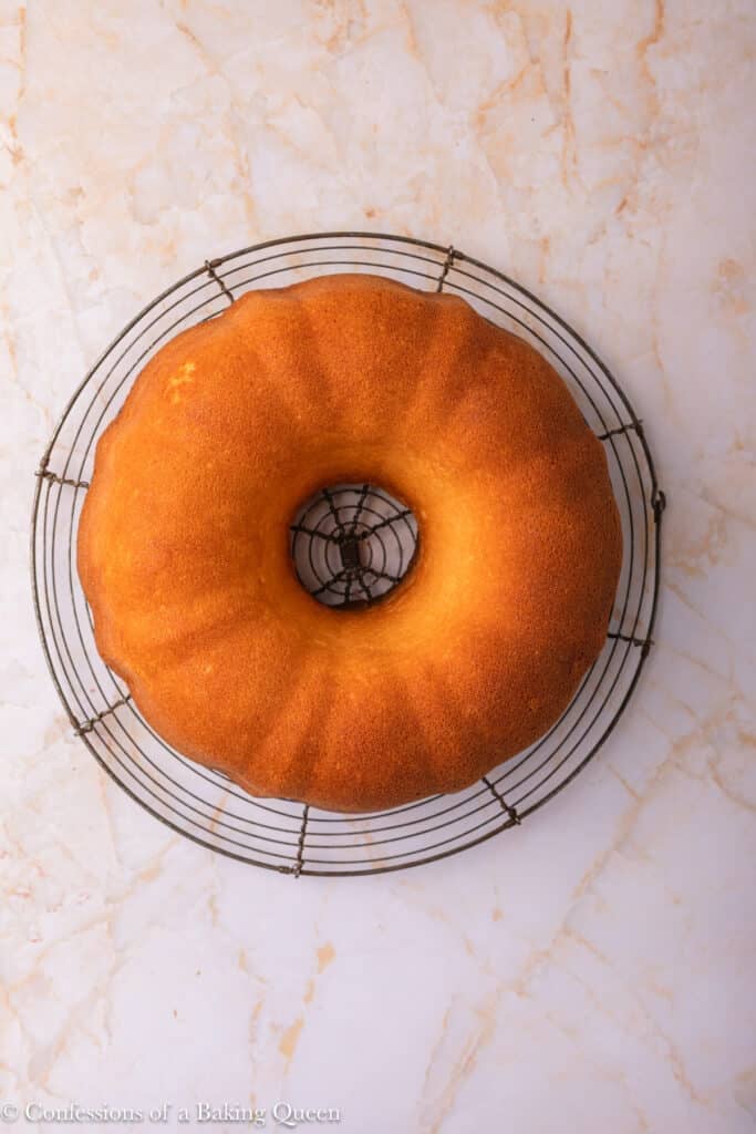 A golden-brown Bundt cake cools on a round wire rack, set on a light marble surface.