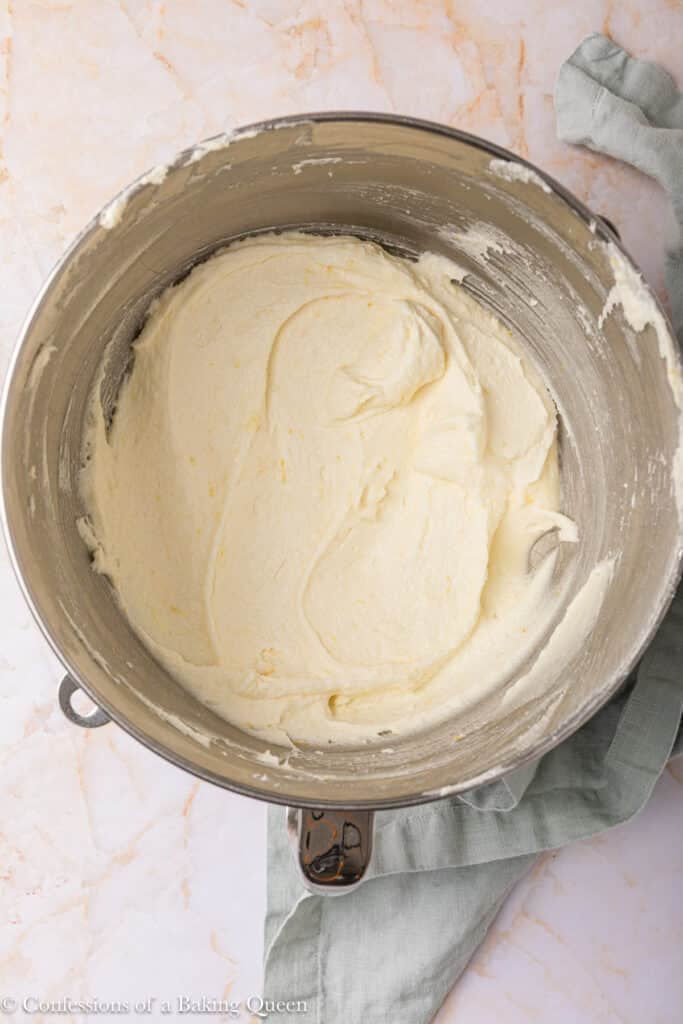 A metal mixing bowl filled with smooth, creamy cake batter sits on a marble surface, with a light green kitchen towel partially visible beside it.