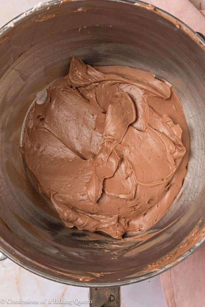 A mixing bowl filled with creamy, smooth chocolate frosting, with spatula marks visible on the surface.